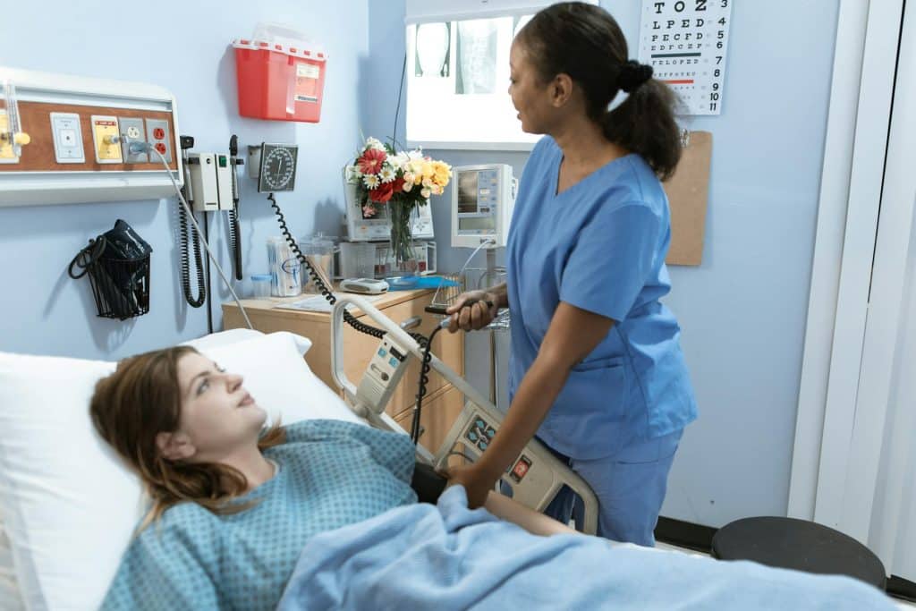Nurse assisting a patient in a hospital bed during bedside imaging care in a clinical ICU-style environment.